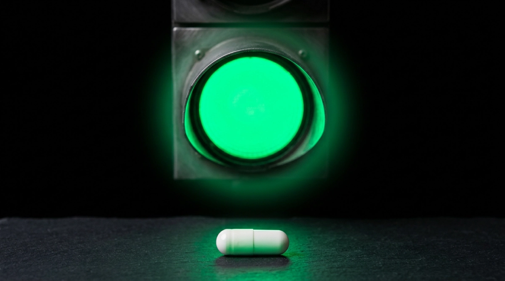 The image features a glowing green traffic light against a black background, with a brushed metal housing that adds a modern touch. Below it, a white pharmaceutical capsule is positioned, reflecting the green glow above, suggesting themes of permission and clearance.