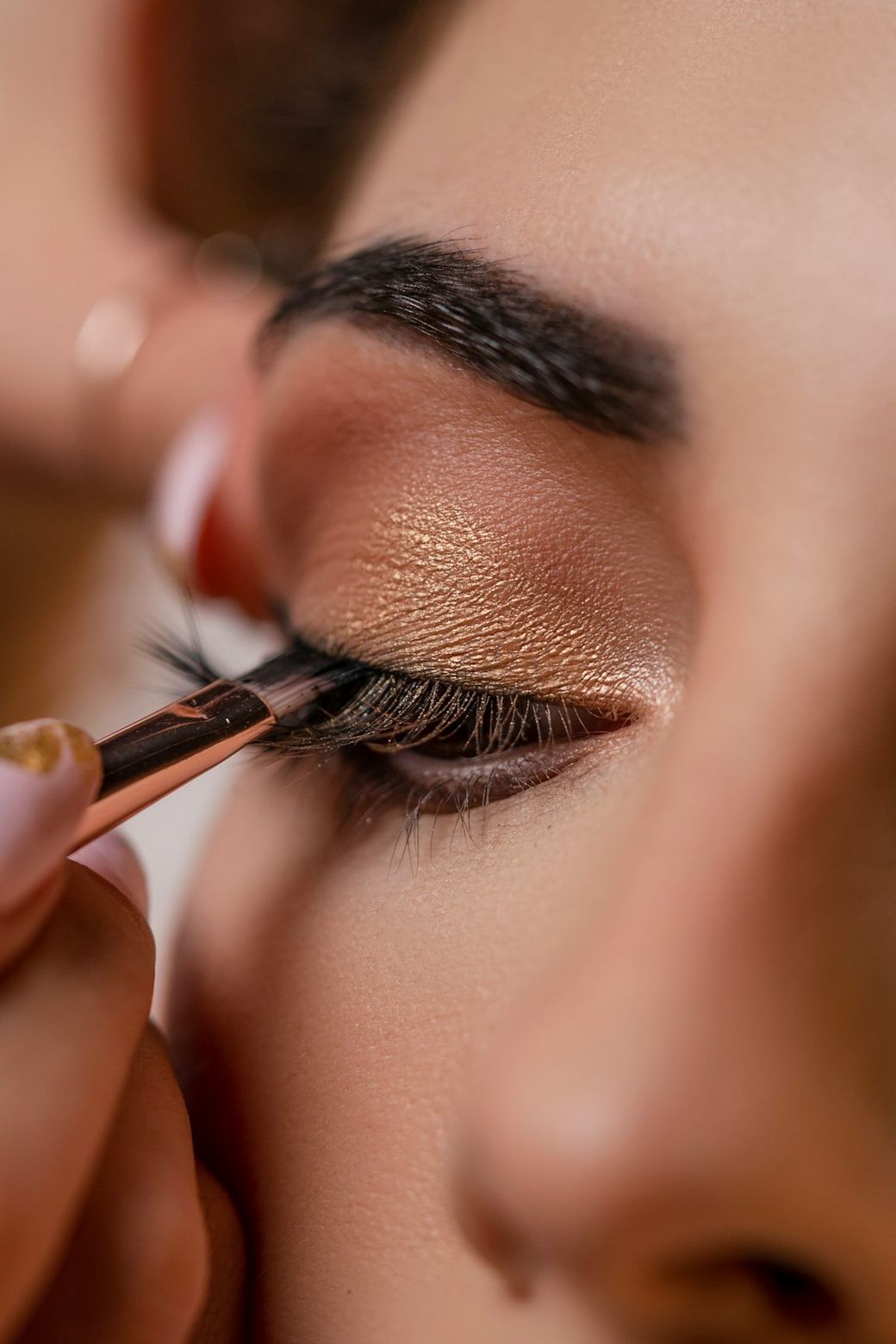 A close-up image of a person applying makeup to another person's eye, focusing on the eyelash application process. The makeup features warm tones and emphasizes the eye area. — Credit: Photo by LOLA AZIZADA on Unsplash