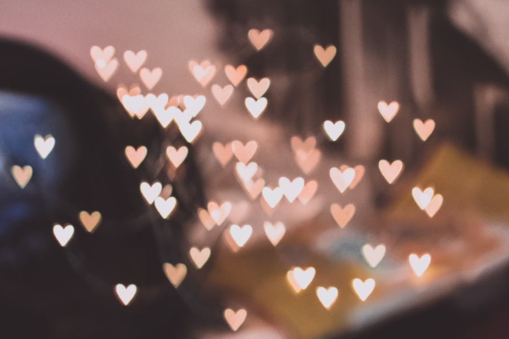 The image features a series of out-of-focus heart-shaped lights, creating a warm and romantic ambiance. The background appears to include blurred furniture or personal items, enhancing the intimate feel of the scene. — Credit: Photo by freestocks on Unsplash