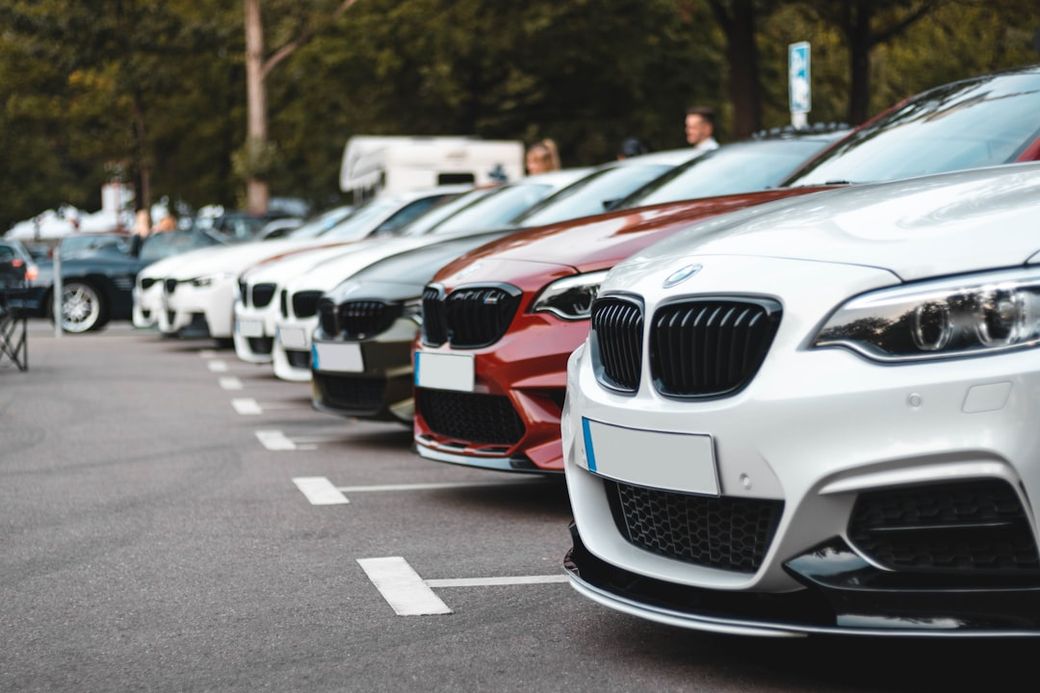 The image features a lineup of several BMW cars parked in a row on a street. The focus is on the front grills and hoods of the vehicles, showcasing their stylish designs. — Credit: Photo by Sara Kurfeß on Unsplash