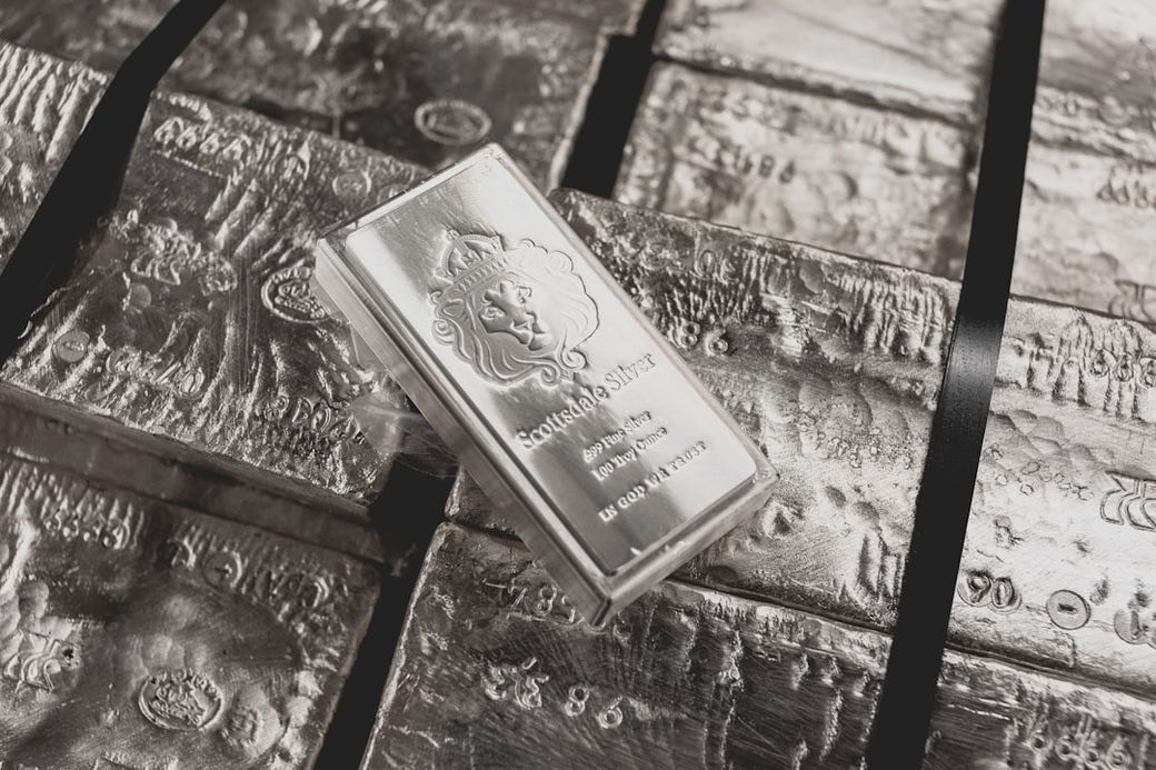 The image features stacked silver bars, prominently displaying a silver ingot labeled 'Scotiabank Silver.' The bars show intricate designs and textures typical of bullion, indicating a focus on precious metals. — Credit: Photo by Scottsdale Mint on Unsplash