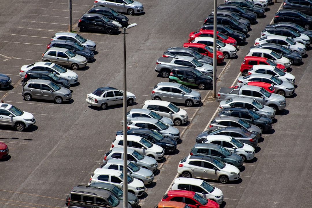 Aerial view of a busy parking lot filled with various parked vehicles. The lot shows a mix of colors and styles of cars parked in orderly rows.