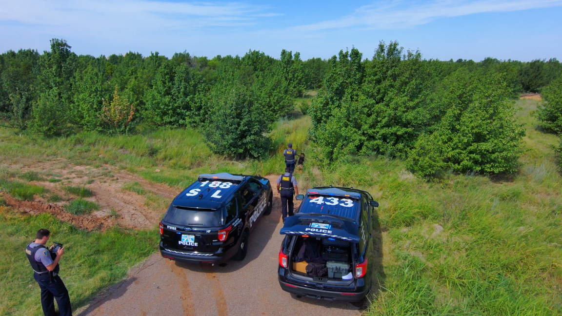 picture of police launching drone in rural wooded field 