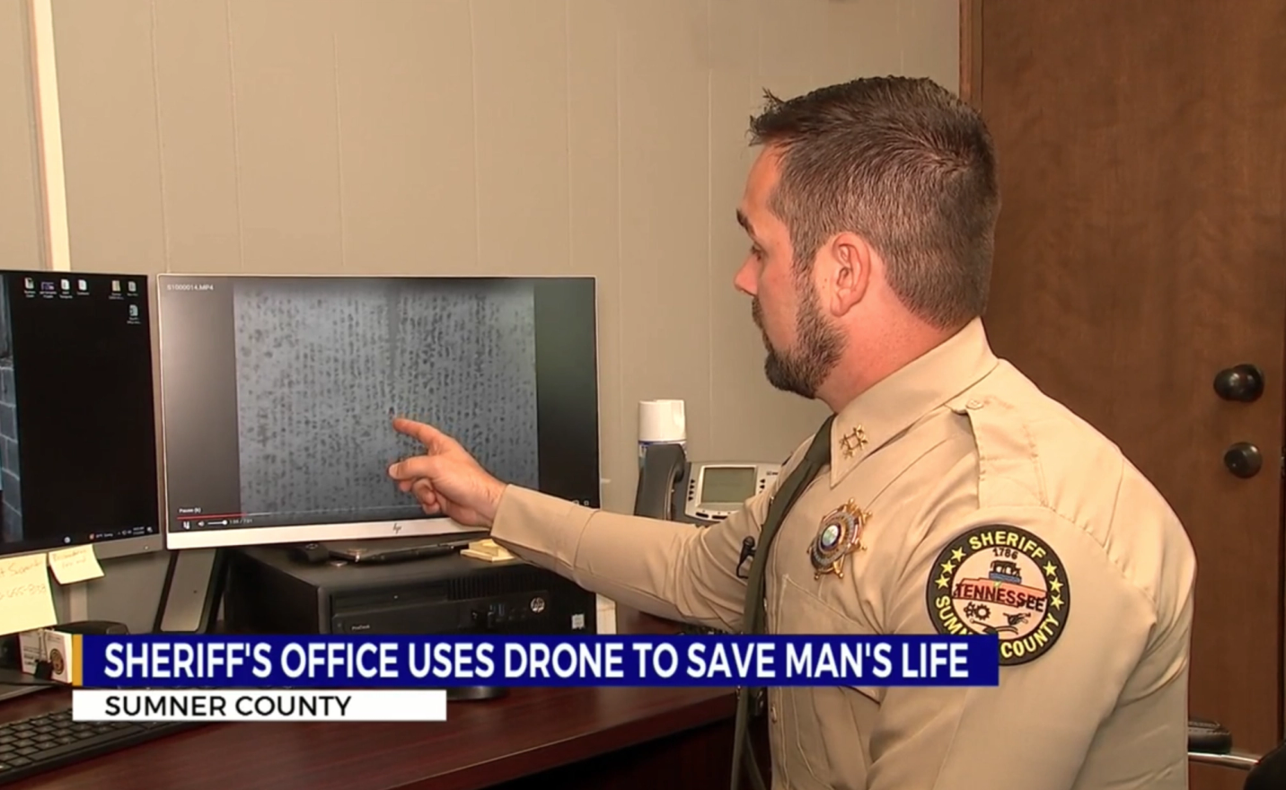 Sheriff's officer to the right of the frame pointing to one of two screens on a desk. The screen shows a video still taken from a Skydio drone.