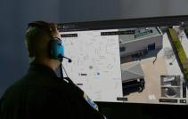 Officer with headset on and back to the camera looking at a large display showing a map on one side and a live video feed from a Skydio drone on the right.