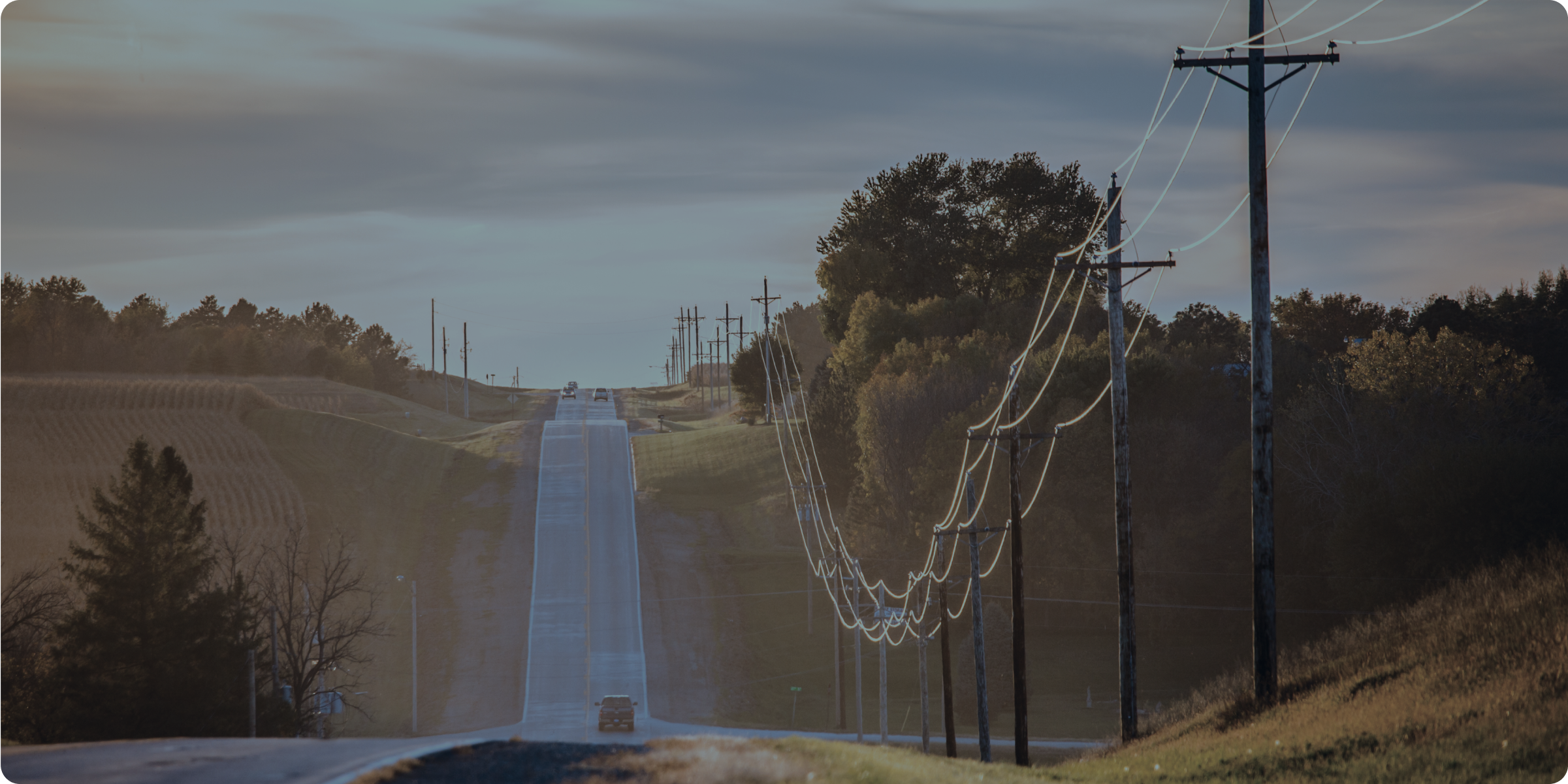 road in countryside with long stretch of electrical poles and wires running beside