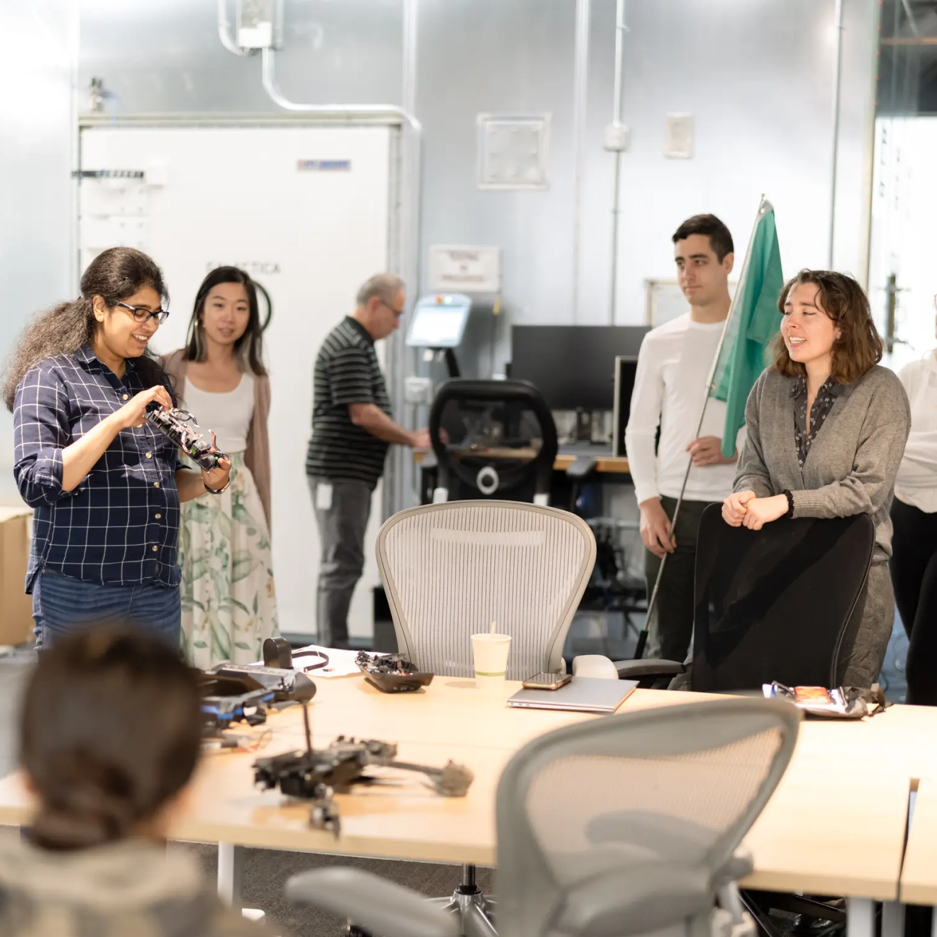 Several students around a table with chairs, one holding a Skydio drone and another drone on the table.