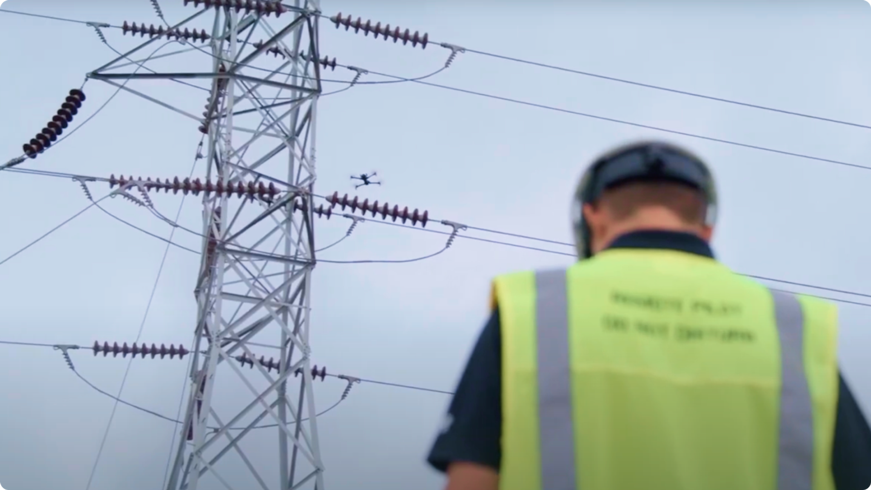 drone operator's back with drone flying a utility inspection near electrical infrastructure