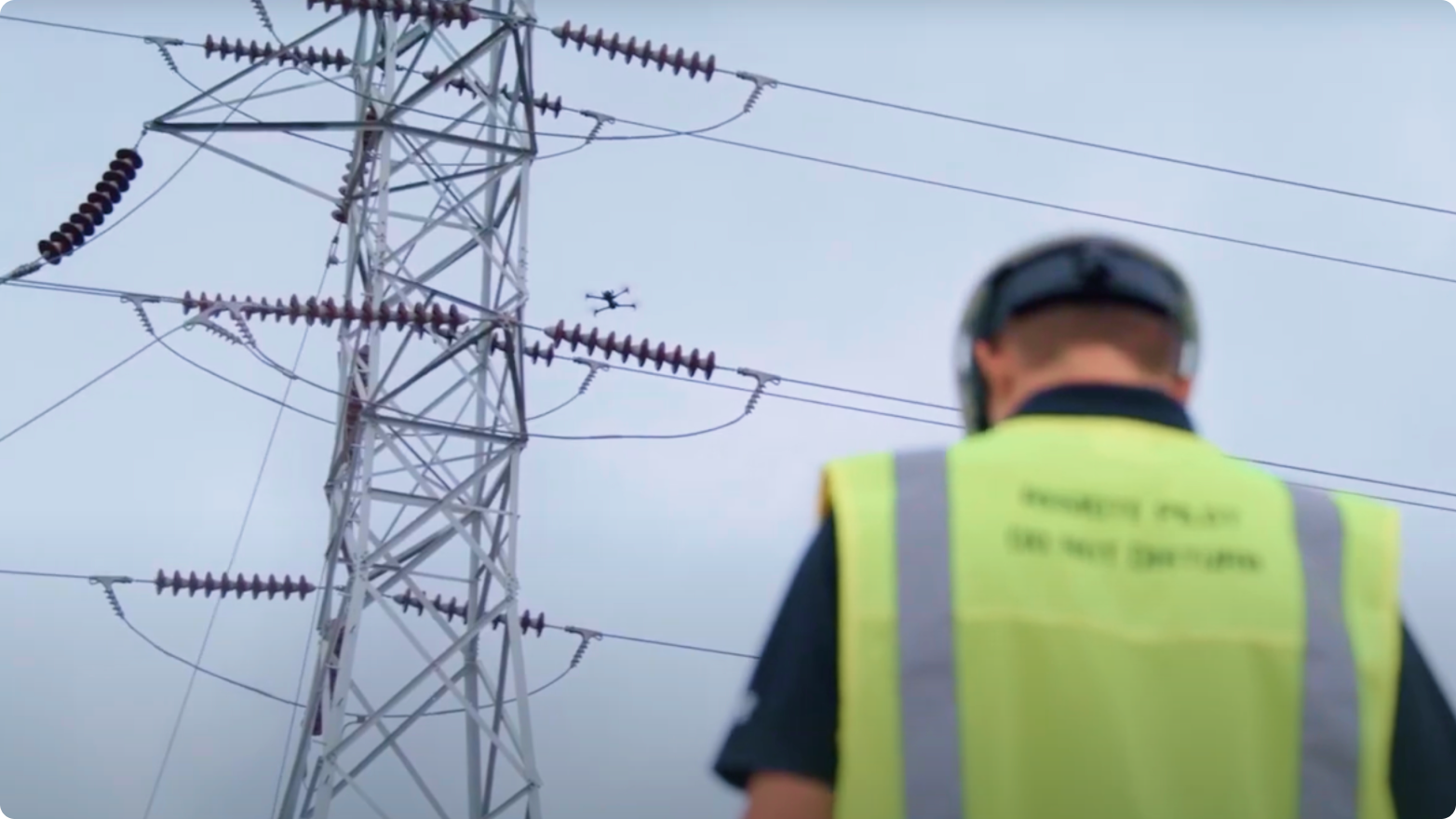 drone operator's back with drone flying a utility inspection near electrical infrastructure