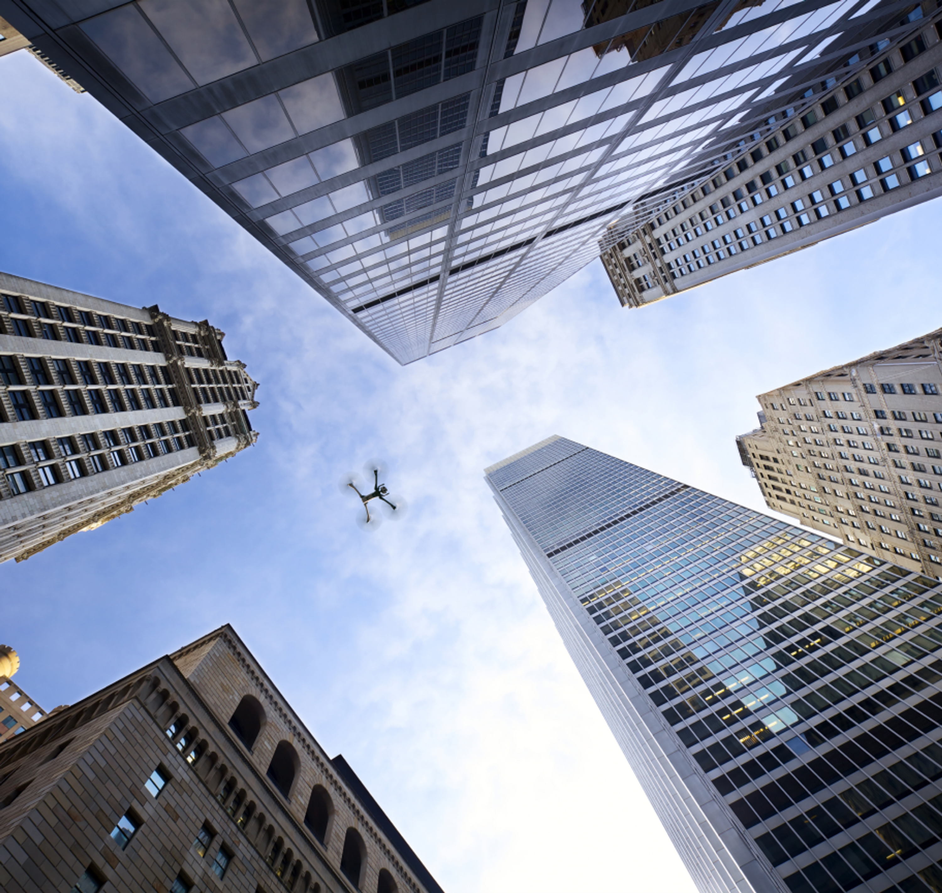 Skydio X10 drone viewed from below, flying high between skyscraper buildings