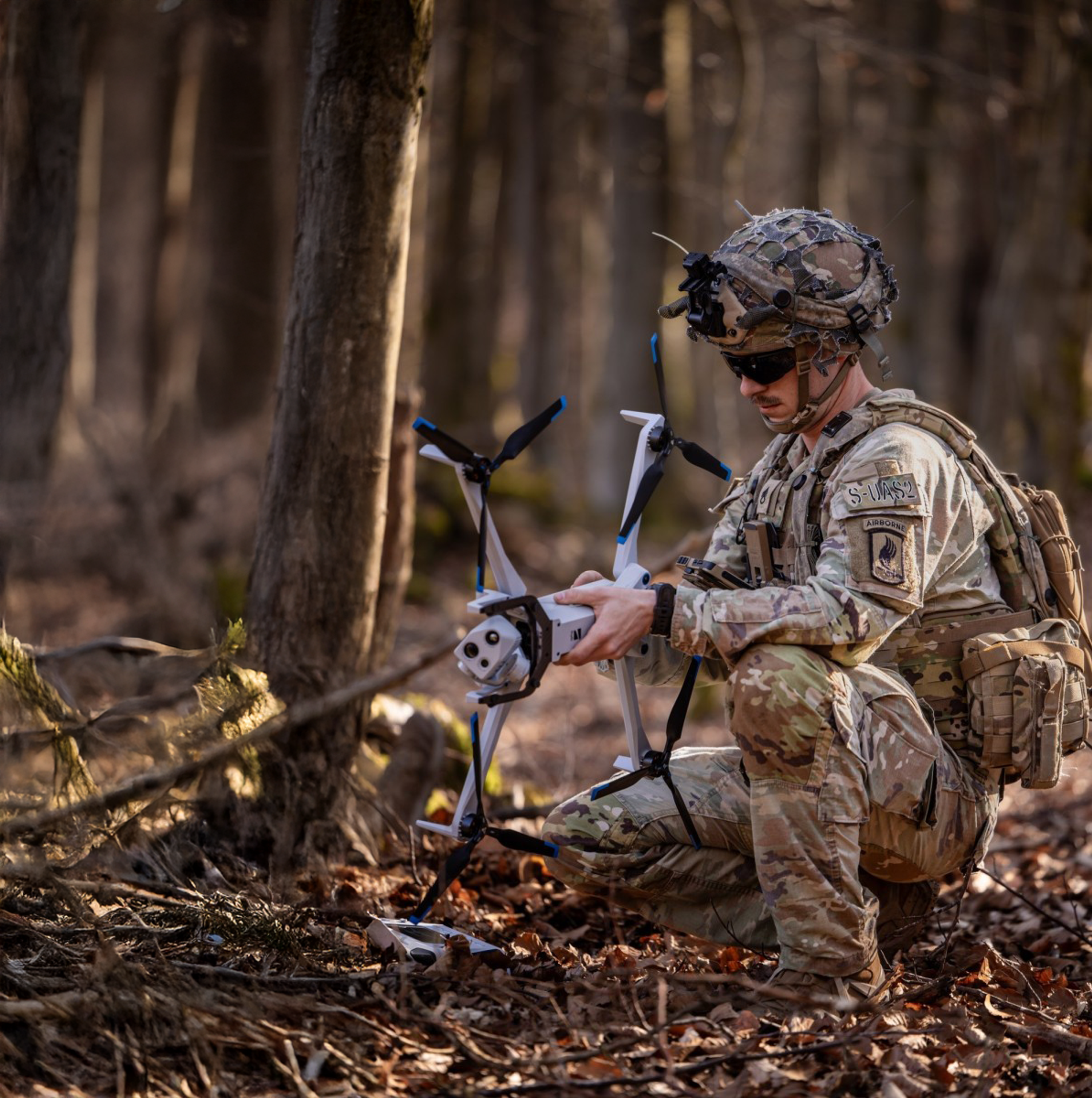 crouching warfighter in the woods with a Skydio X10D drone in hand
