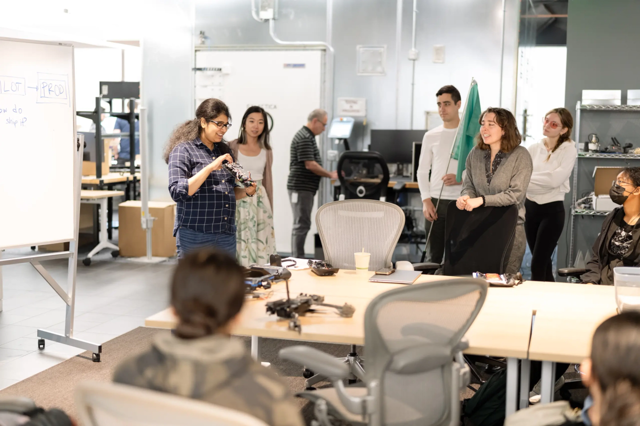 Several students around a table with chairs, one holding a Skydio drone and another drone on the table.