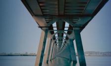 A concrete bridge over water with multiple sets of identical pillars, photo taken under the bridge facing in its direction going across the water