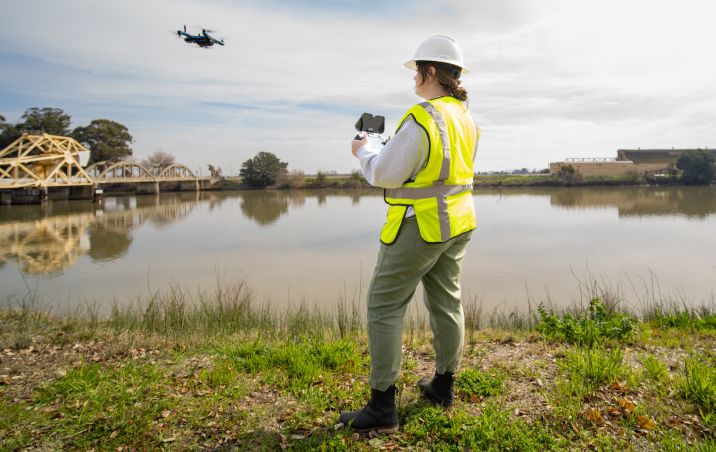 worker on site using skydio controller to inspect bridge in background.