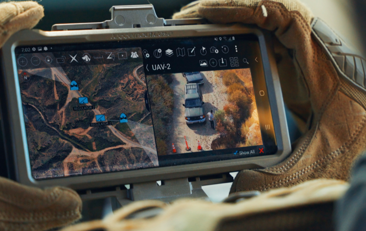 Soldier looking at chest tablet of live feed of Skydio X10D observing convoy at road block