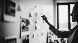 A hand reaches toward a wall covered with notes, suggesting creative planning or active brainstorming in a workspace.