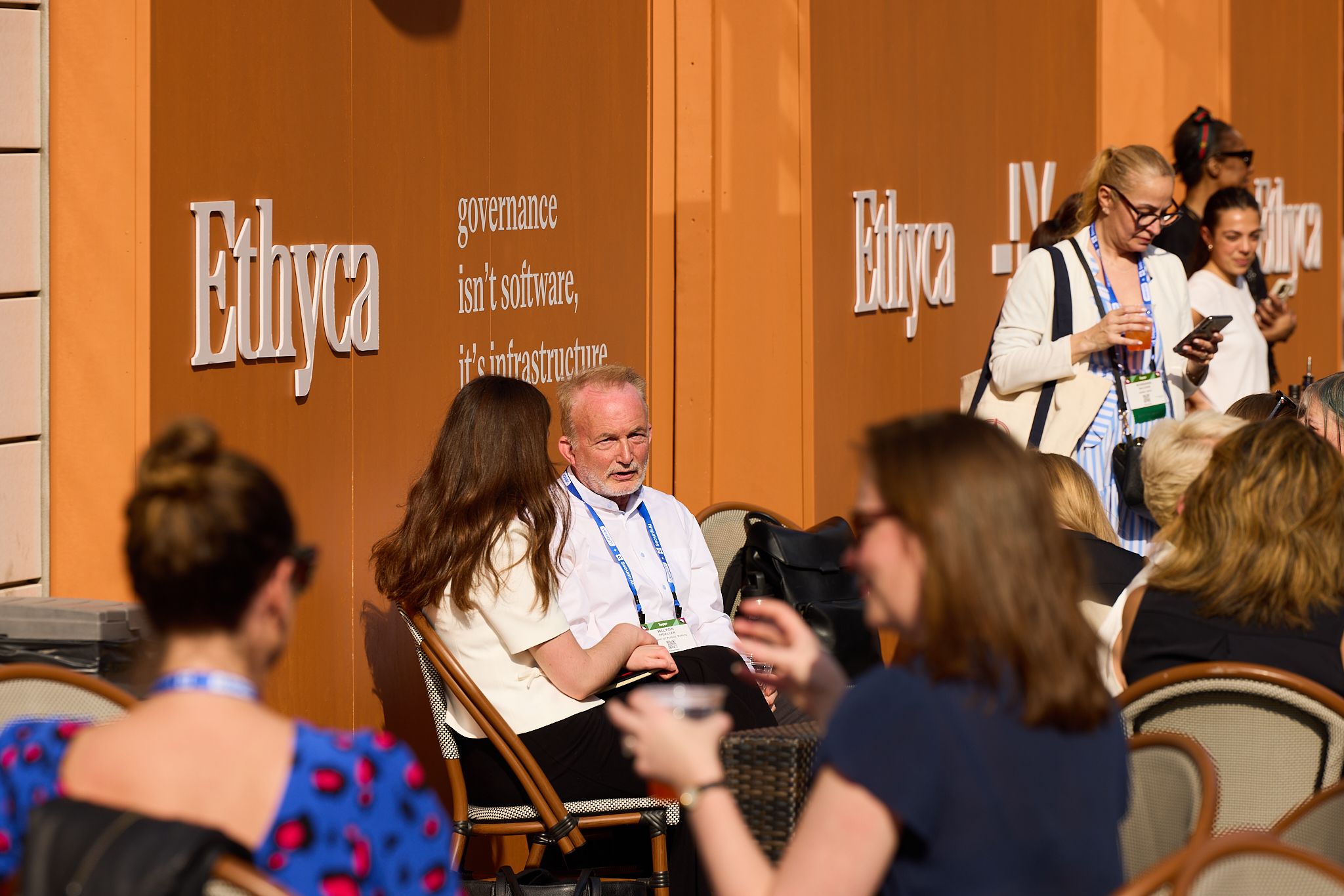 People sitting outside inn cafe chairs with Ethyca branding on an orange wall.