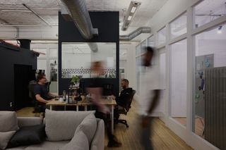Blurred figures walking in front of desks with people in a loft-style office.