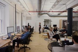 A brightly lit studio with computers on the wall and people working with motion blur