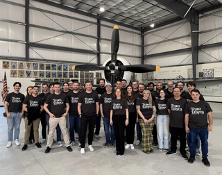 A group of people standing in front of a fighter place in a hangar