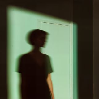 Blurred silhouette against a green-hued wall, creating an abstract and mysterious atmosphere with soft lighting and shadows