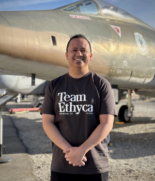 A man with a black shirt standing in front of a jet fighter