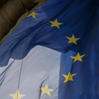 A large European Union flag flowing in the wind surrounded by classical stone arches.