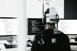 Monochrome image of a coder working on a dark-themed interface, with headphones and a futuristic digital distortion effect.