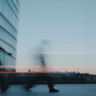 Blurred figure walking in a modern cityscape at sunset, with sleek architecture and a serene sky.