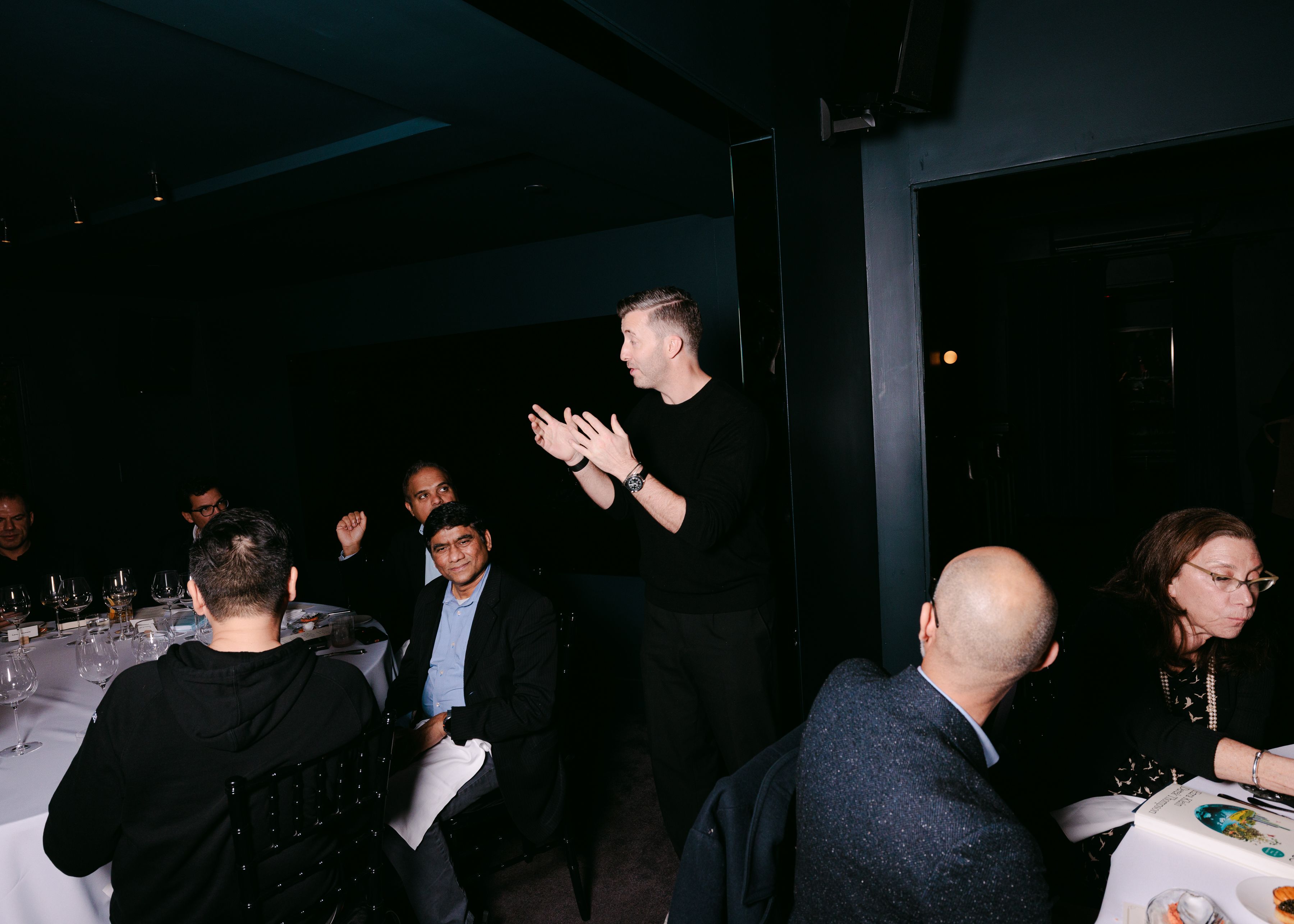 A man giving a presentation in front of two dinner tables.