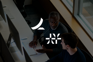 Two people sitting at a computer debating in an office setting in front of a window.