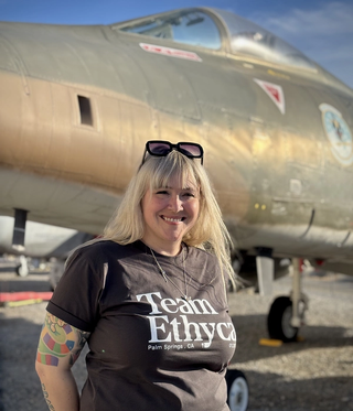 A woman with tattoos with a black shirt standing in front of a jet fighter
