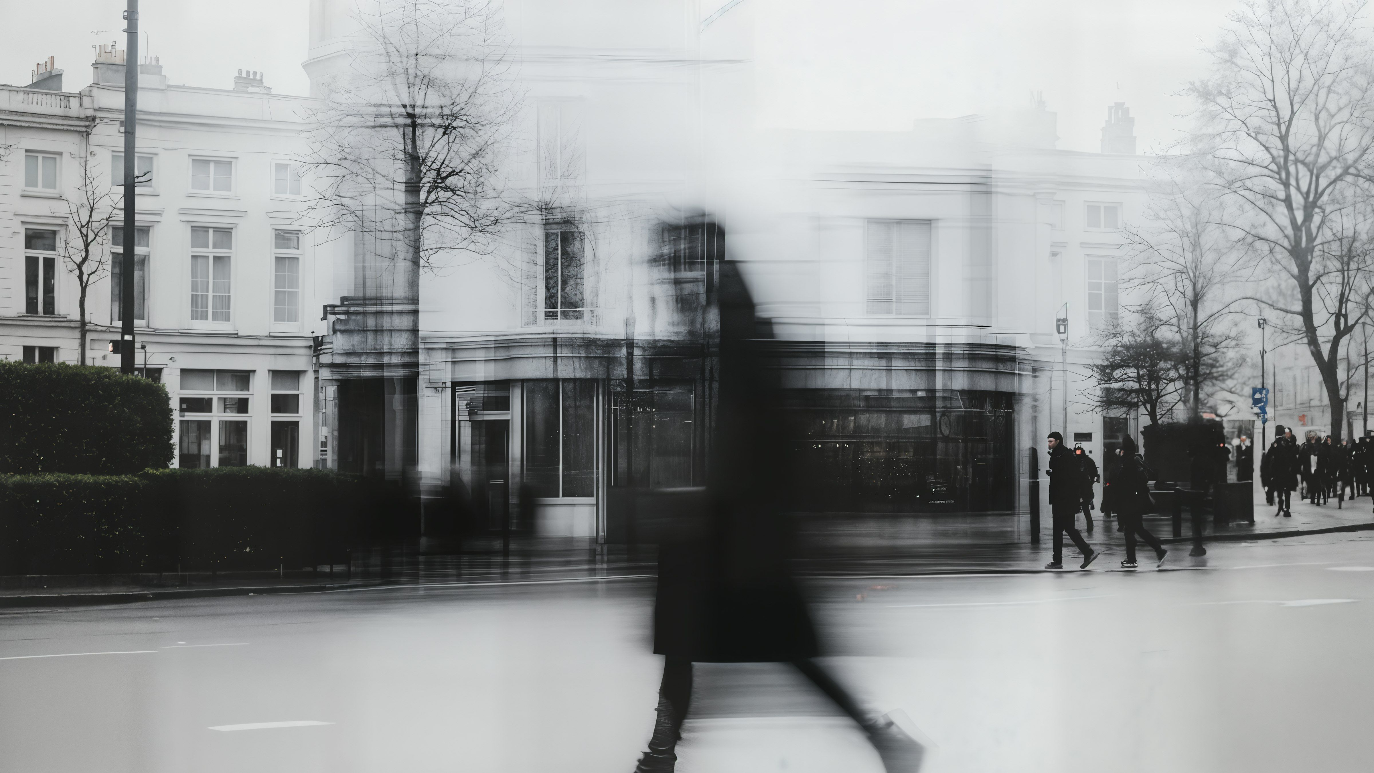 Blurred black-and-white image of a person walking in an urban setting, emphasizing motion and a minimalist aesthetic