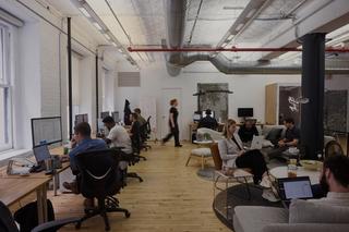 A brightly lit studio with computers on the wall and people working with motion blur