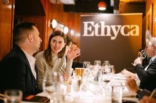 Two people talking at a long dinner table with an Ethyca banner.