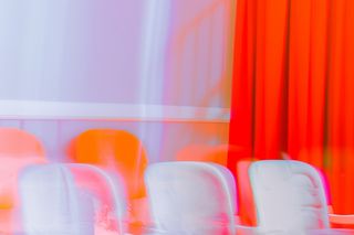 Abstract image of white chairs with motion blur, set against a bold red curtain