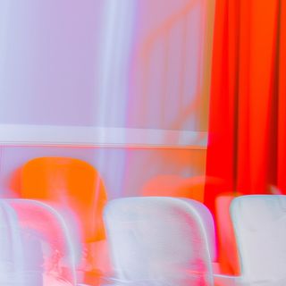 Abstract image of white chairs with motion blur, set against a bold red curtain