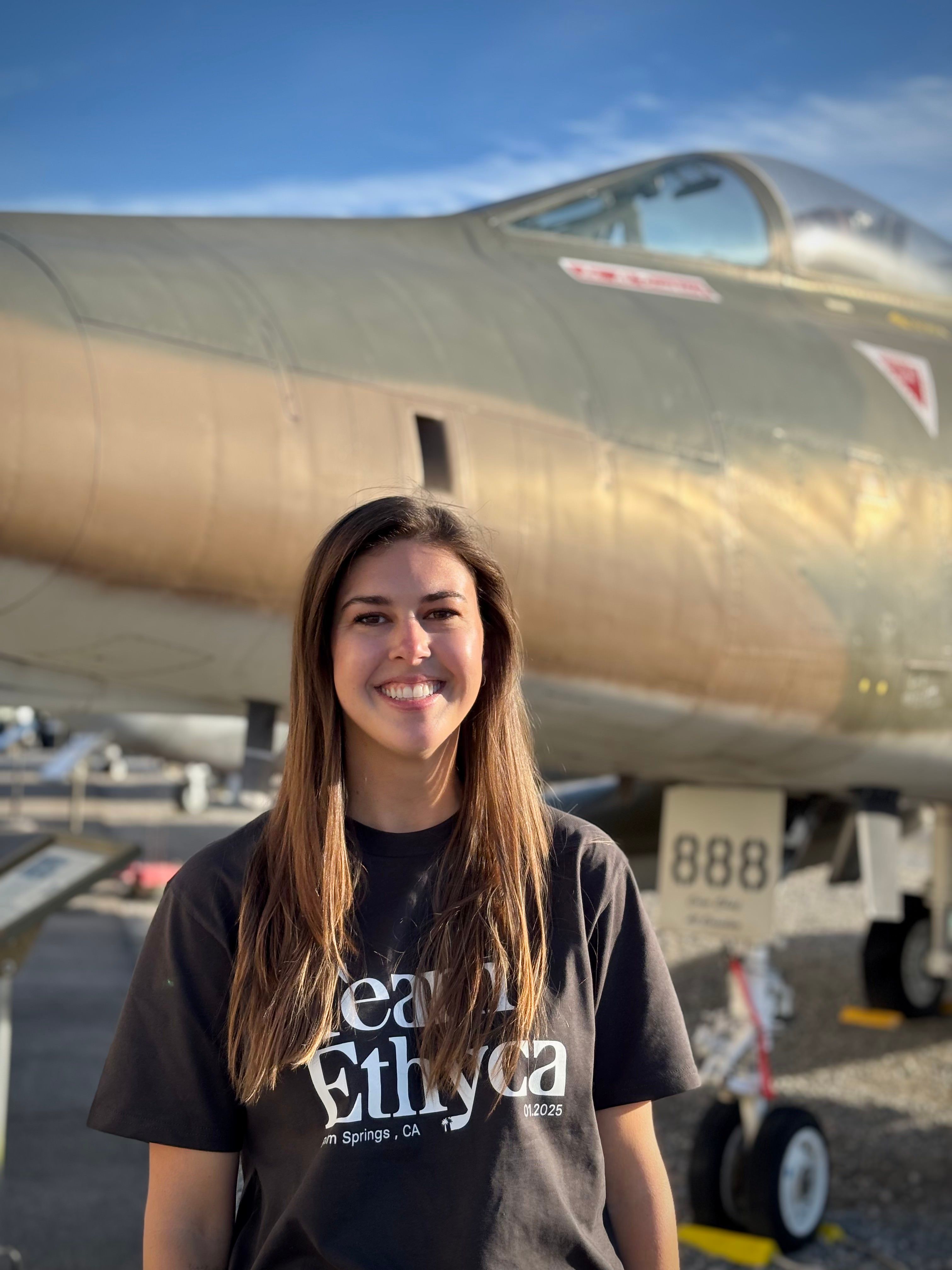 A woman with a black shirt and standing in front of a jet fighter