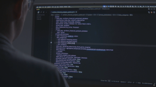 A person sitting in front of a computer screen with code.