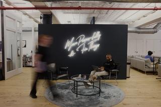 Office environment with people walking in front of a blue wall.