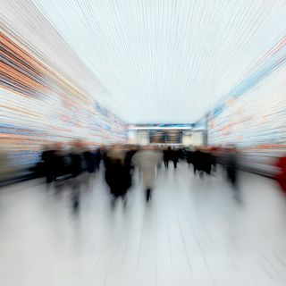 Blurred motion of people in a vibrant, futuristic terminal with colorful digital displays and a bright, tiled floor
