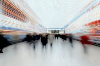 Blurred motion of people in a vibrant, futuristic terminal with colorful digital displays and a bright, tiled floor