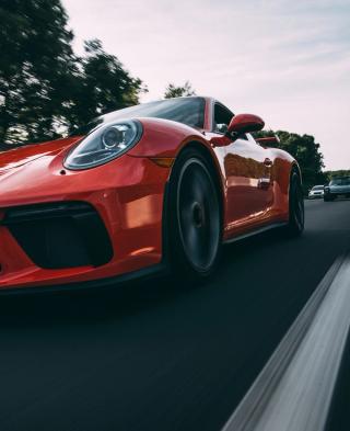 A red Porsche being followed by cars on a racetrack at dusk.