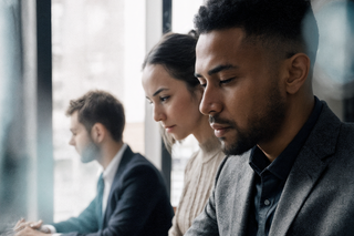 Three people looking focused at work, in a corporate office with large windows looking out onto a city.