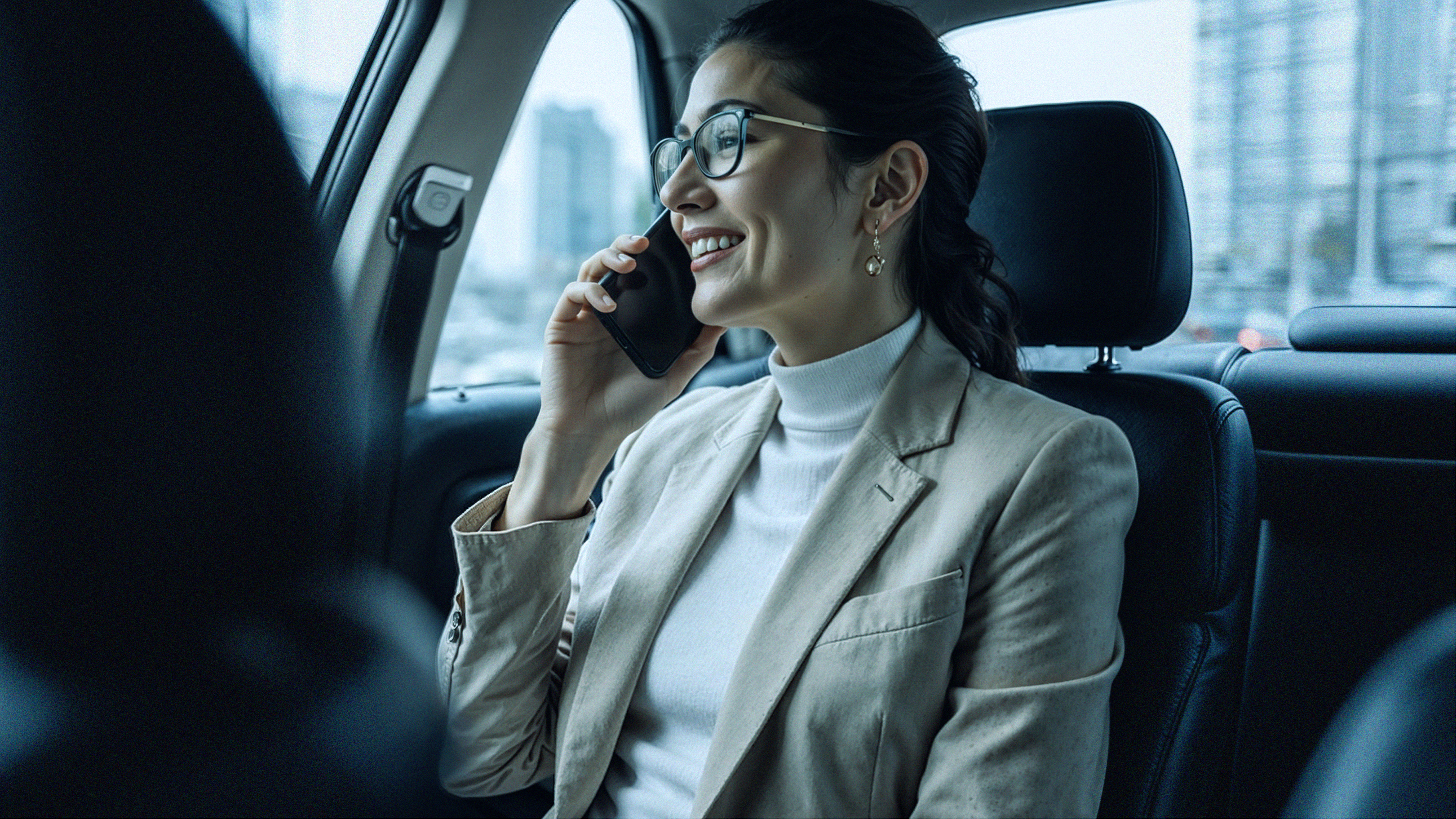 A woman in a beige blazer works at a desk with papers and a laptop, viewed through a partially open door in a dimly lit room.
