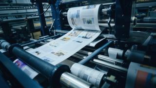 A high-speed printing press produces colorful, detailed magazines, showcasing images and text in a dynamic, industrial setting with a focused, modern tone.
