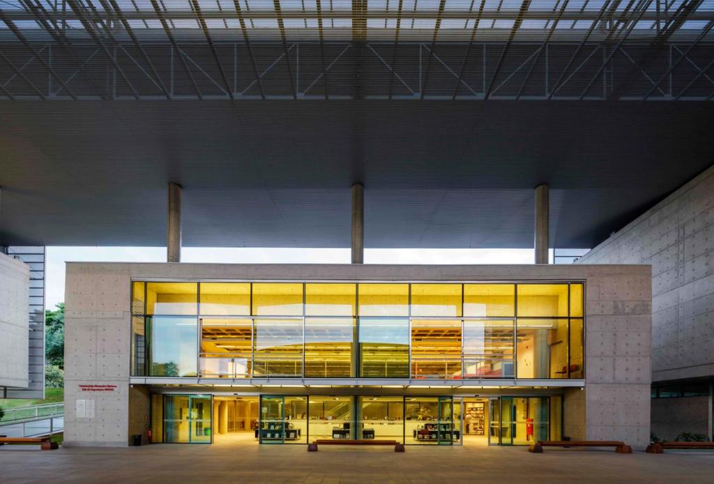 The yellow-lit facade of the Brasiliana Library beneath a concrete canopy, seen from the entrance in the evening