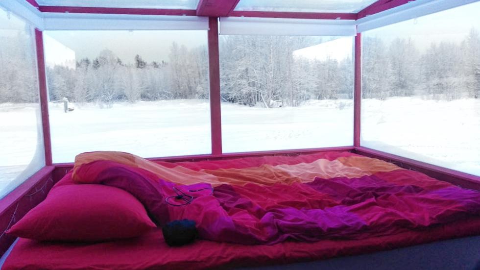 Интерьер домика Lake Inari с яркой розовой постелью и панорамными окнами в зимний пейзаж