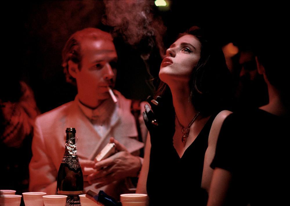 A woman with a cigarette at a bar table, red lighting, a bottle of champagne