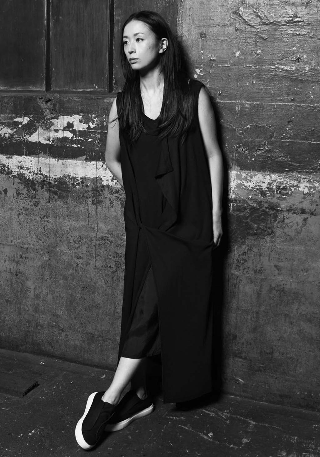 A woman in a sleeveless black dress against a weathered wall, black-and-white photograph
